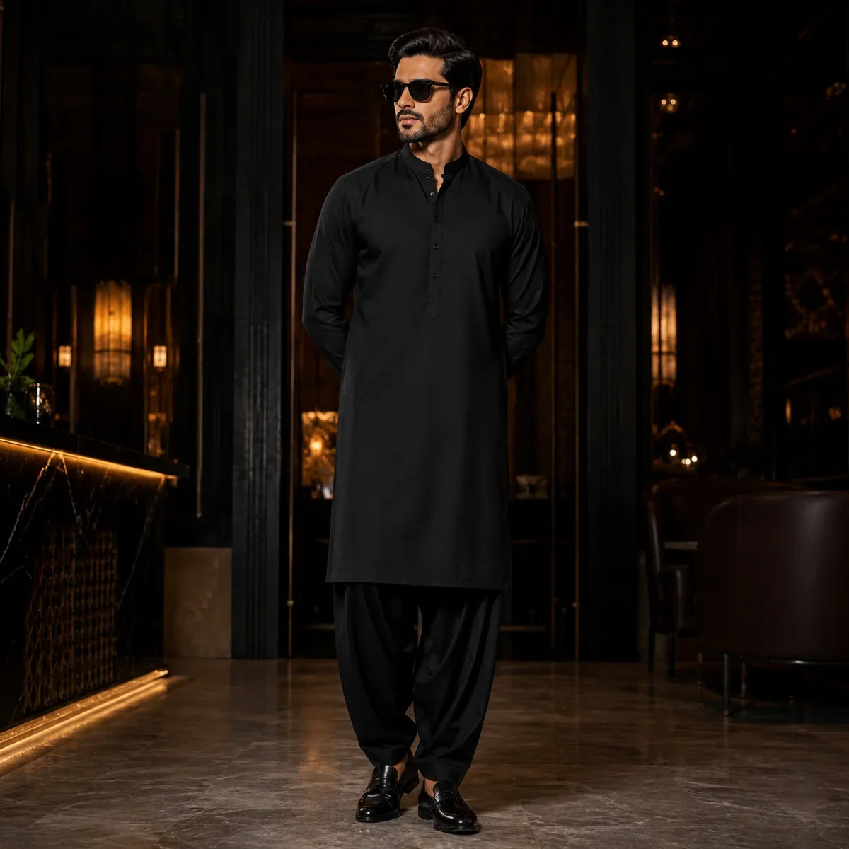 Man in black shalwar kameez for formal wear, styled with sunglasses and loafers in luxury setting