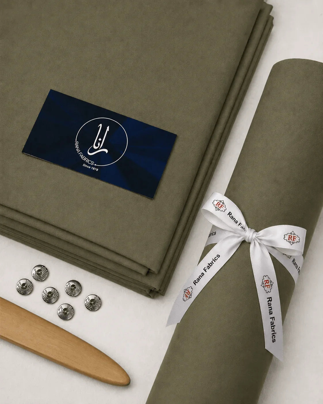 Olive green men's suiting fabric roll with Rana Fabrics ribbon, buttons, and wooden tool for formal wear